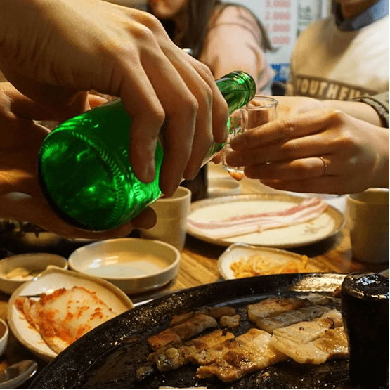 Soju poured from a green bottle into a small glass at a Korean barbecue table